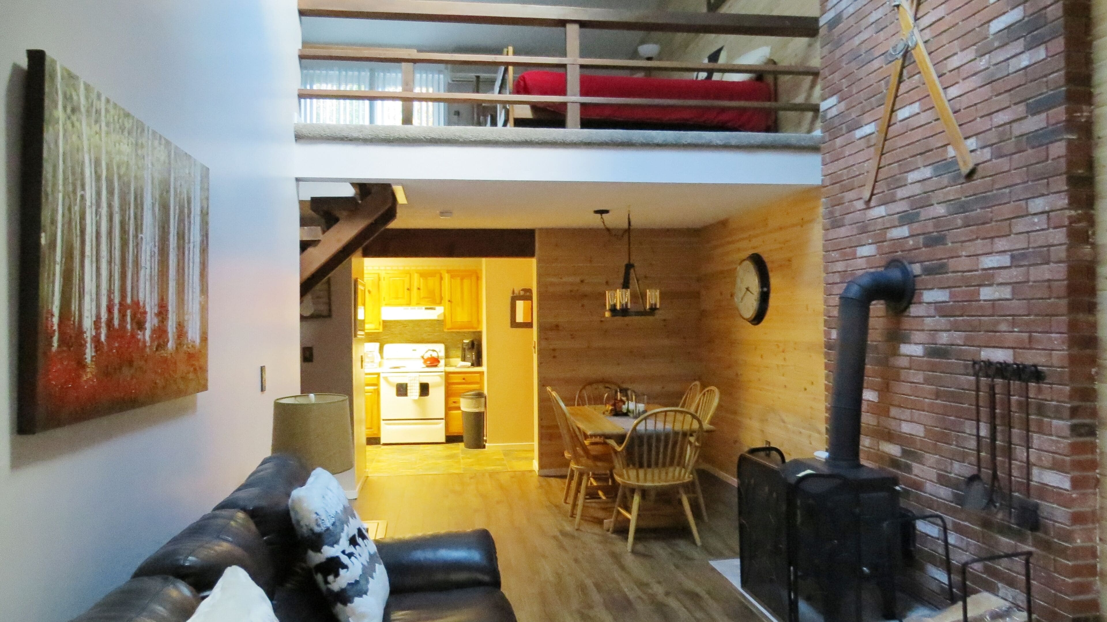 Un espacio habitable tipo loft con comedor, cocina y un dormitorio superior con cama roja.