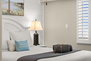 Een keurig opgemaakt bed met kussens, een bedlampje en een raam met zonwering.