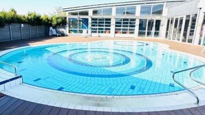 Una piscina con cubierta de madera, rodeada por un edificio con grandes ventanales.