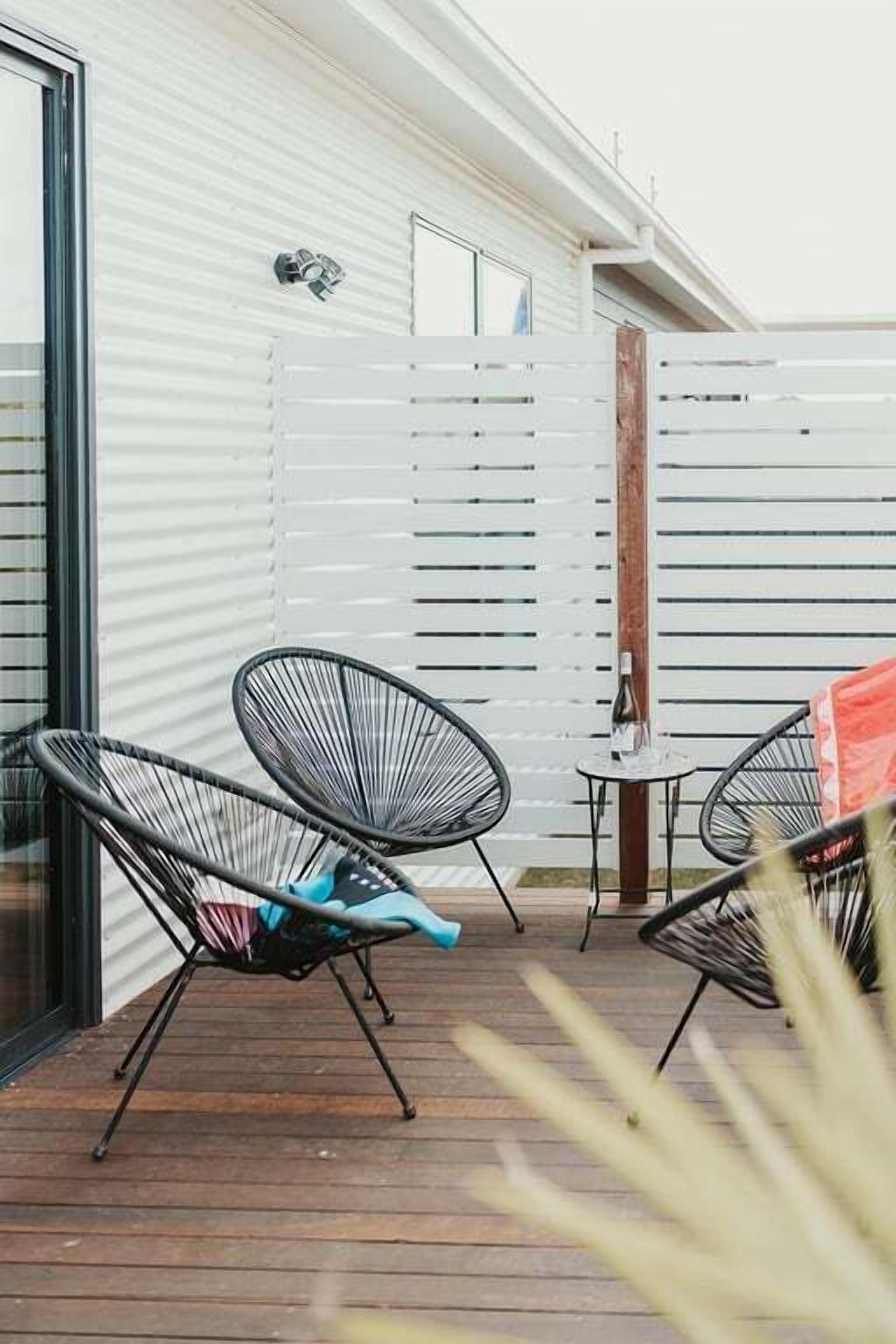 A patio with two black wireframe chairs, a small table, and a bottle.