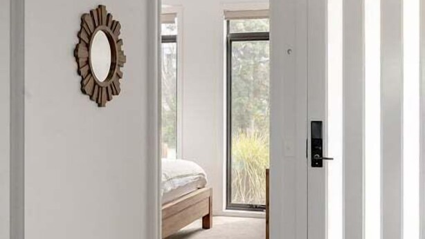 Un pasillo con suelo de madera, una puerta blanca con listones verticales y un espejo en la pared.