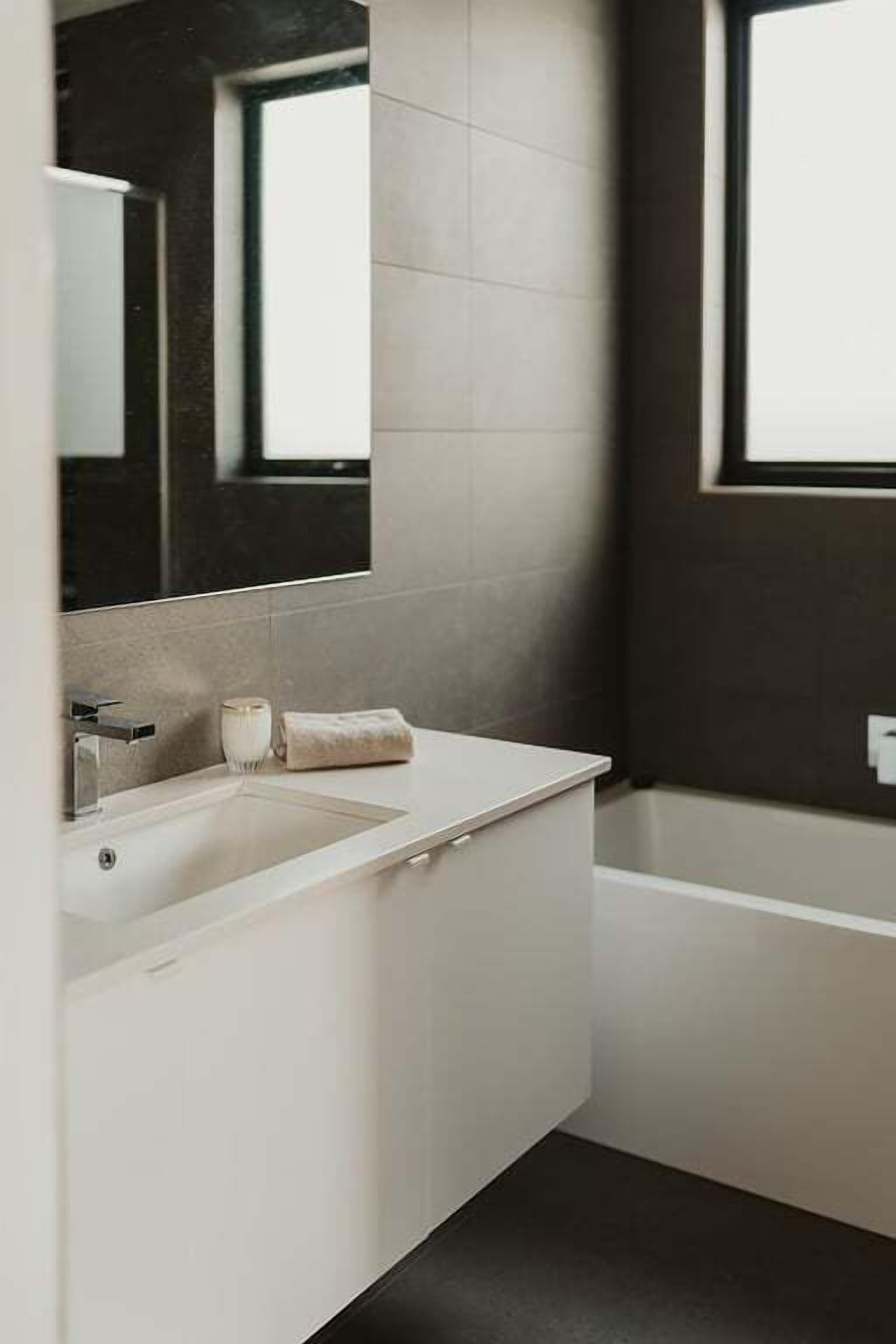 A modern bathroom with a white vanity, a large mirror, a bathtub, and a window.