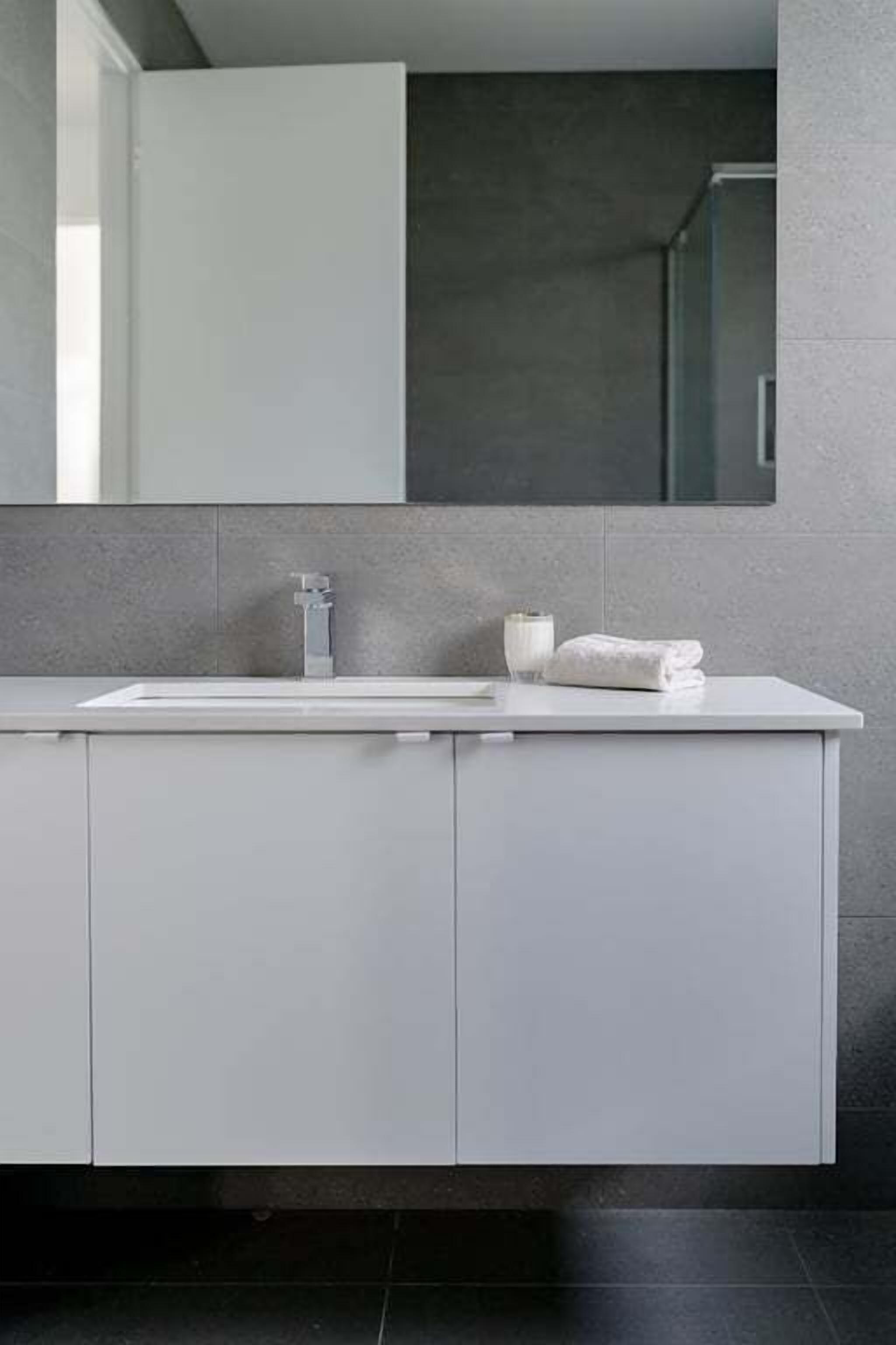 A modern bathroom with a white sink, a mirror above it, and a towel on the counter.