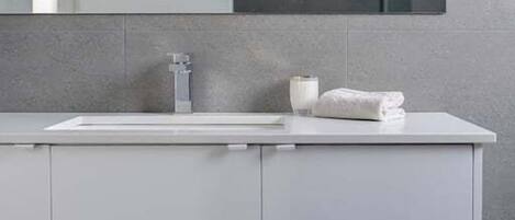 A modern bathroom with a white sink, a mirror above it, and a towel on the counter.