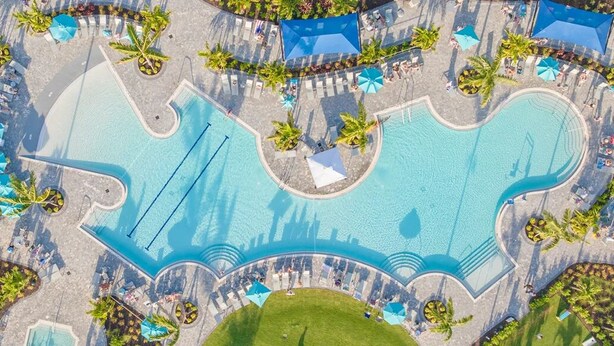 Ein Luftbild von einem Poolbereich mit einem herzförmigen Design, umgeben von Liegestühlen und Sonnenschirmen.