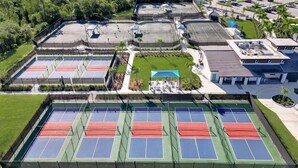 Eine Vogelperspektive auf eine Sportanlage mit mehreren Tennisplätzen, einem Schwimmbad und umliegender Bepflanzung.