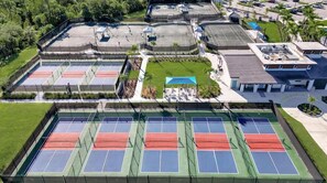 An aerial view of a sports facility with multiple tennis courts, a swimming pool, and surrounding greenery. - Luxury Beach & Golf Retreat: New 2BR/2BA, Resort Amenities, 15 Mins to Beach! (Venice)