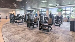 Ein Fitnessraum mit Trainingsgeräten, großen Fenstern und einem Fischgrätparkett.
