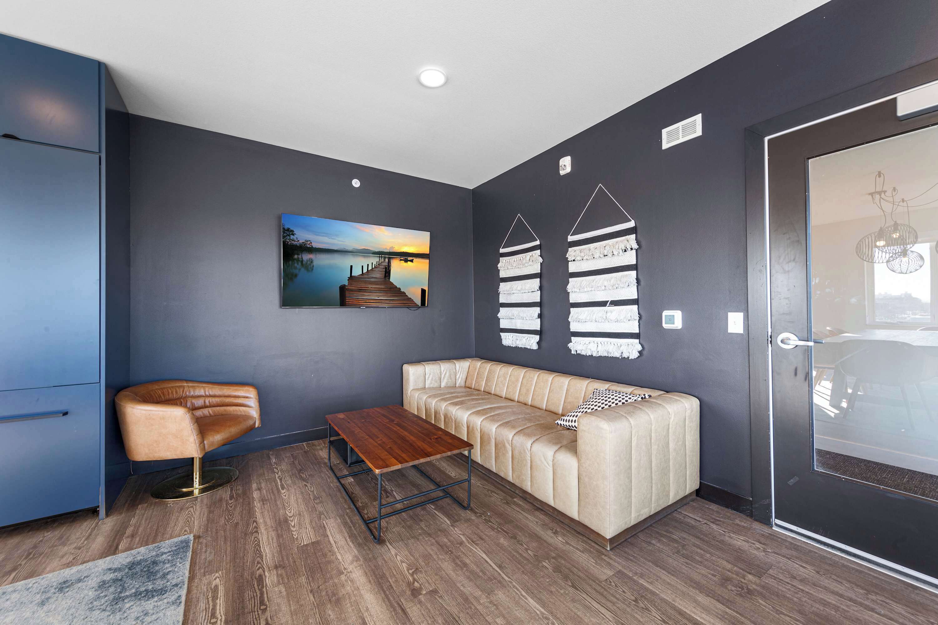 A modern living room with a sofa, a coffee table, and a chair. There is a painting on the wall and a door with a glass panel.