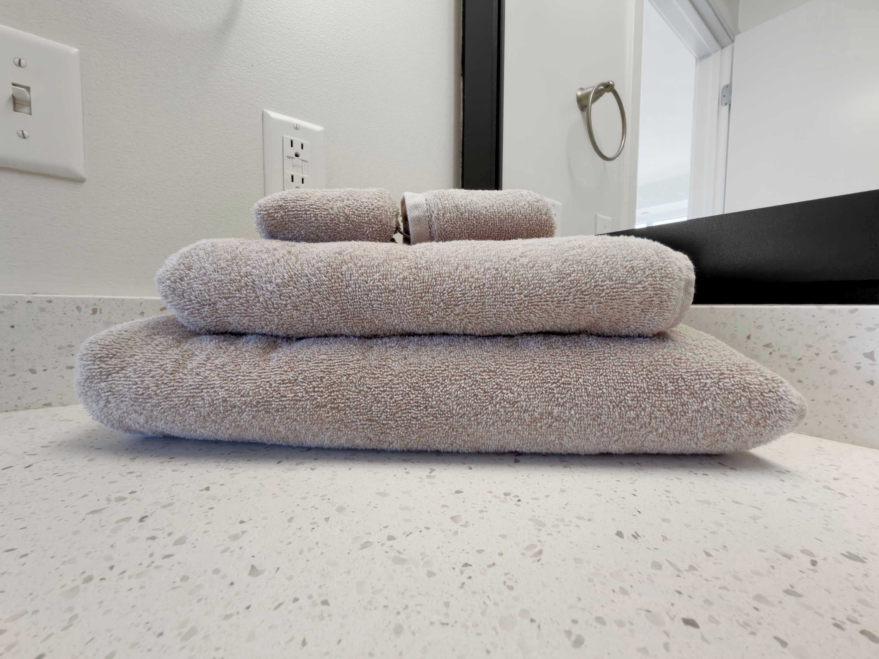 A bathroom with a white countertop, a towel rack, and a towel folded on the counter.