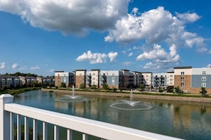 Un quartier résidentiel avec des immeubles à plusieurs étages, un plan d’eau agrémenté de fontaines et un ciel dégagé.
