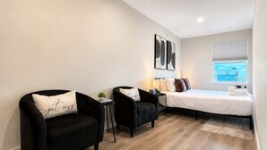 Quarto moderno com uma cama, duas poltronas pretas, uma mesinha e uma janela com vista.