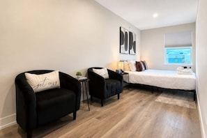 A modern bedroom with a bed, two black armchairs, a small table, and a window with a view. - 4BR Warrenville Home w/ Patio & Garage, Sleeps 10 (Warrenville)