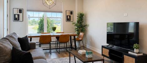 A modern living room with a sofa, dining table, chairs, a TV, and a large window.