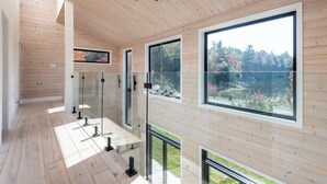 Um interior moderno com painéis de madeira, janelas amplas e guarda-corpo de vidro com vista para um jardim.