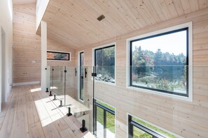 Ein modernes Interieur mit Holzwandverkleidung, großen Fenstern und einem Glasgeländer mit Blick auf einen Garten.