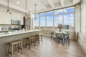 A modern kitchen with a large island, bar stools, and a dining area with a view of the city. - Skyline Atlanta Stay | King Suites + Pool (Atlanta)