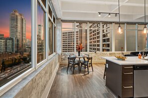 A modern kitchen with a large island, a dining area with a table and chairs, and a view of a cityscape through large windows. - Skyline Atlanta Stay | King Suites + Pool (Atlanta)