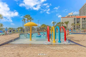 A swimming pool with colorful water features, palm trees, and a building in the background. - Sand Dunes 1044 (Myrtle Beach)