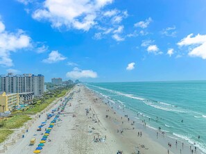 A beach with a row of colorful umbrellas, a sandy shore, and buildings in the background. - Sand Dunes 1044 (Myrtle Beach)