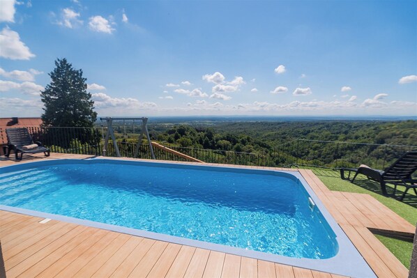 A swimming pool with a wooden deck, a slide, and a view of the landscape. - Villa in nature with jacuzzi, sauna, pool, barbecue, and entertainment amenities (Orešje Okićko)