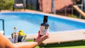 Una persona sostiene una botella de aceite de oliva Canolle Masiacovano cerca de una piscina.