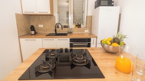 Una cocina moderna con estufa negra, armarios blancos, un lavamanos de acero inoxidable y un frutero sobre la encimera.