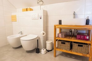 A bathroom with two toilets, bidets, a toilet paper holder, a trash bin, a shelf with wicker baskets, and a soap dispenser. - Villa in nature with jacuzzi, sauna, pool, barbecue, and entertainment amenities (Orešje Okićko)