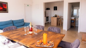 Un comedor con mesa de madera, sofá azul y cocina al fondo.