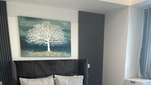 Ein modernes Schlafzimmer mit einem großen Bett, einem Baumgemälde, einem Nachttisch und einer Kommode.