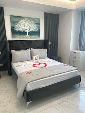 Een moderne slaapkamer met een groot bed, een schilderij van een boom, een nachtkastje en een dressoir.