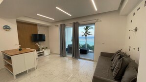 Ein modernes Wohnzimmer mit Fernseher, einer Holzkabine, einer Couch und Meerblick durch eine Schiebetür.
