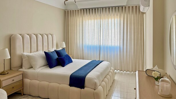 A hotel room with a large bed, a bedside table with a lamp, a nightstand, a wooden dresser, and a window with curtains. - The Overlook Tangier - Panoramic Sea and Kasbah View Downtown (Tanger)
