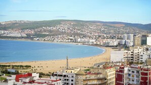 A coastal cityscape with a beach, buildings, and wind turbines in the background. - The Overlook Tangier - Panoramic Sea and Kasbah View Downtown (Tanger)