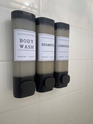 Three bottles of body wash, shampoo, and conditioner mounted on a wall. - Beautiful Home in Moreno Valley (Moreno Valley)