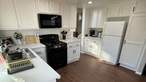 A modern kitchen with white cabinetry, a black stove, a microwave, and a refrigerator. - Beautiful Home in Moreno Valley (Moreno Valley)