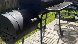 Una parrilla con chimenea, una mesa de metal y una carretilla en un patio trasero.
