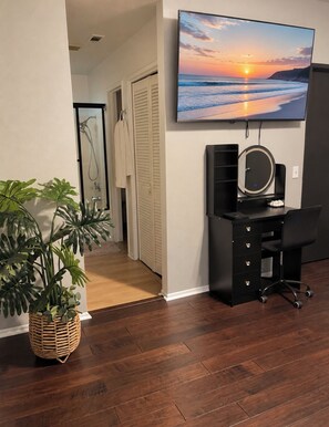 A room with a wooden floor, a desk with a chair, a television mounted on the wall, and a potted plant. - Beautiful Home in Moreno Valley (Moreno Valley)