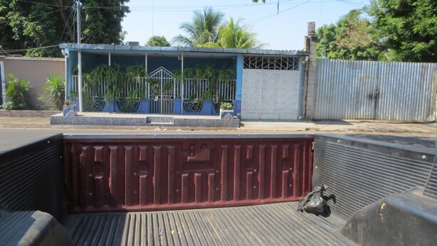 Un conteneur métallique rouge à la surface texturée, un bâtiment bleu avec une porte en métal et, au fond, une clôture métallique.