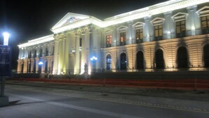 Un grand bâtiment de style classique, doté de colonnes et de fenêtres en arc de cercle, illuminé la nuit.