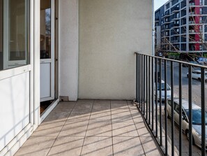 Ein Balkon mit Fliesenboden, einem Metallgeländer und Blick auf geparkte Autos sowie Gebäude im Hintergrund.