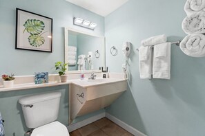 A bathroom with a toilet, sink, mirror, towel rack, and a framed plant. - Shores of Panama - Gulf Views - 2BR + Bunks - Beach Chairs Included (Panama City Beach)