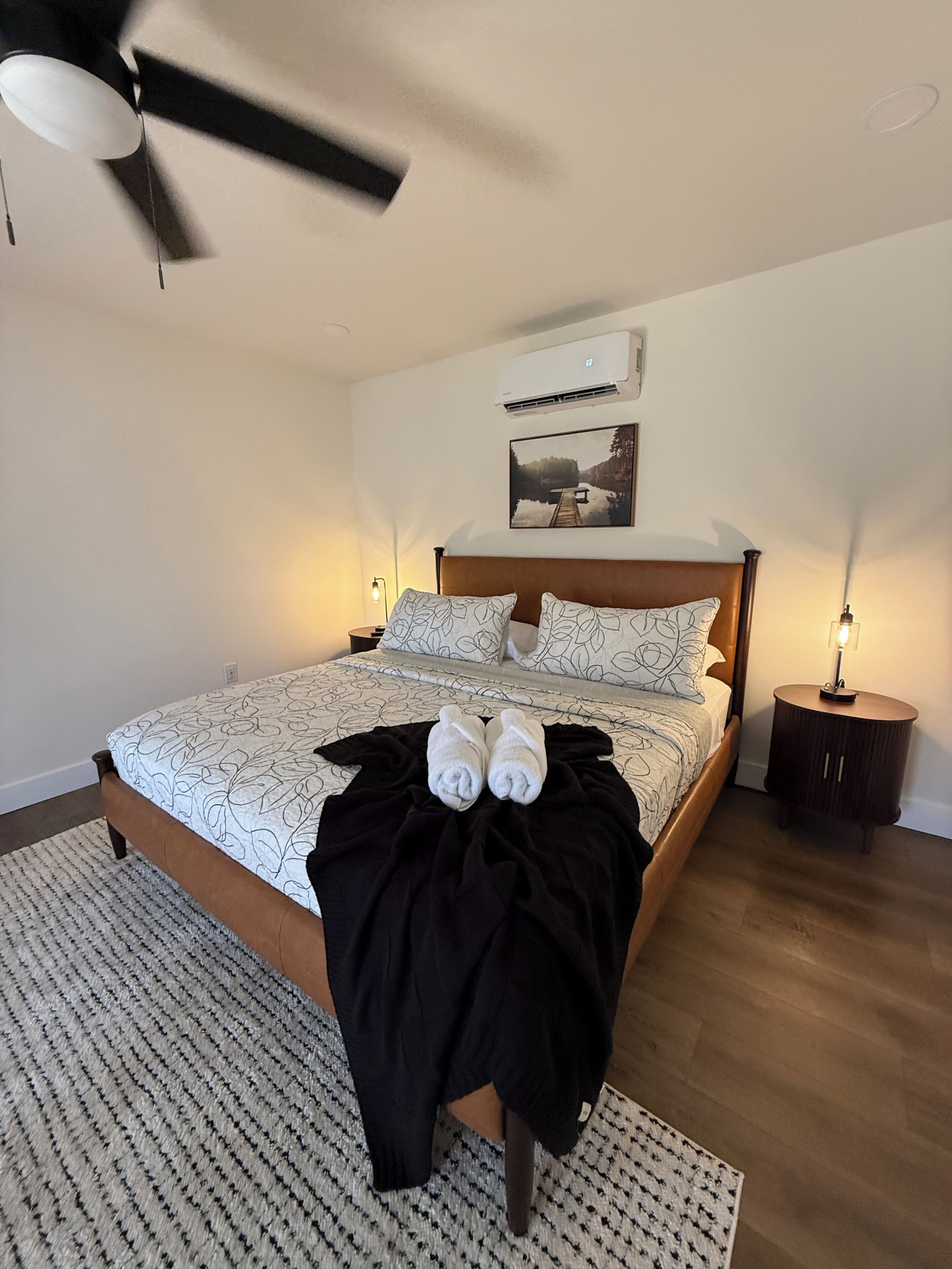 Une chambre à coucher comprenant un lit, un ventilateur de plafond, un appareil de climatisation, une table de chevet avec une lampe et un tapis.