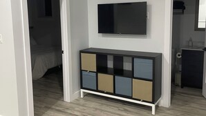 A room with a wooden floor, a white door, a black TV on the wall, and a multi-colored cabinet. - Cozy two-bedroom basement apartment equipped with a full kitchen! (Min 28 days) (Lake Loon)