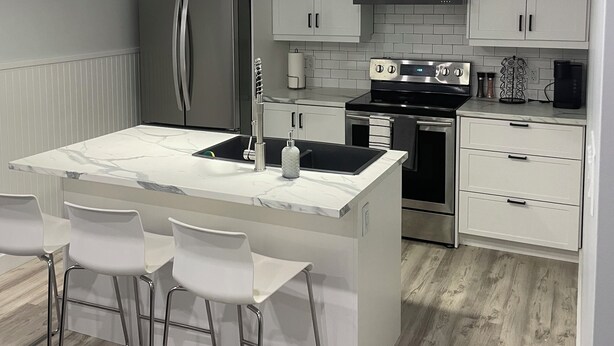 A modern kitchen with white cabinetry, a marble island, stainless steel appliances, and pendant lighting. - Cozy two-bedroom basement apartment equipped with a full kitchen! (Min 28 days) (Lake Loon)