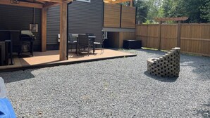 A covered patio with a grill, outdoor seating, and a stack of bricks. - Cozy two-bedroom basement apartment equipped with a full kitchen! (Min 28 days) (Lake Loon)