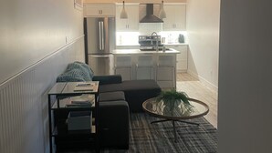 A modern kitchen with white cabinets, stainless steel appliances, pendant lighting, and a dining area with a table and chairs. - Cozy two-bedroom basement apartment equipped with a full kitchen! (Min 28 days) (Lake Loon)