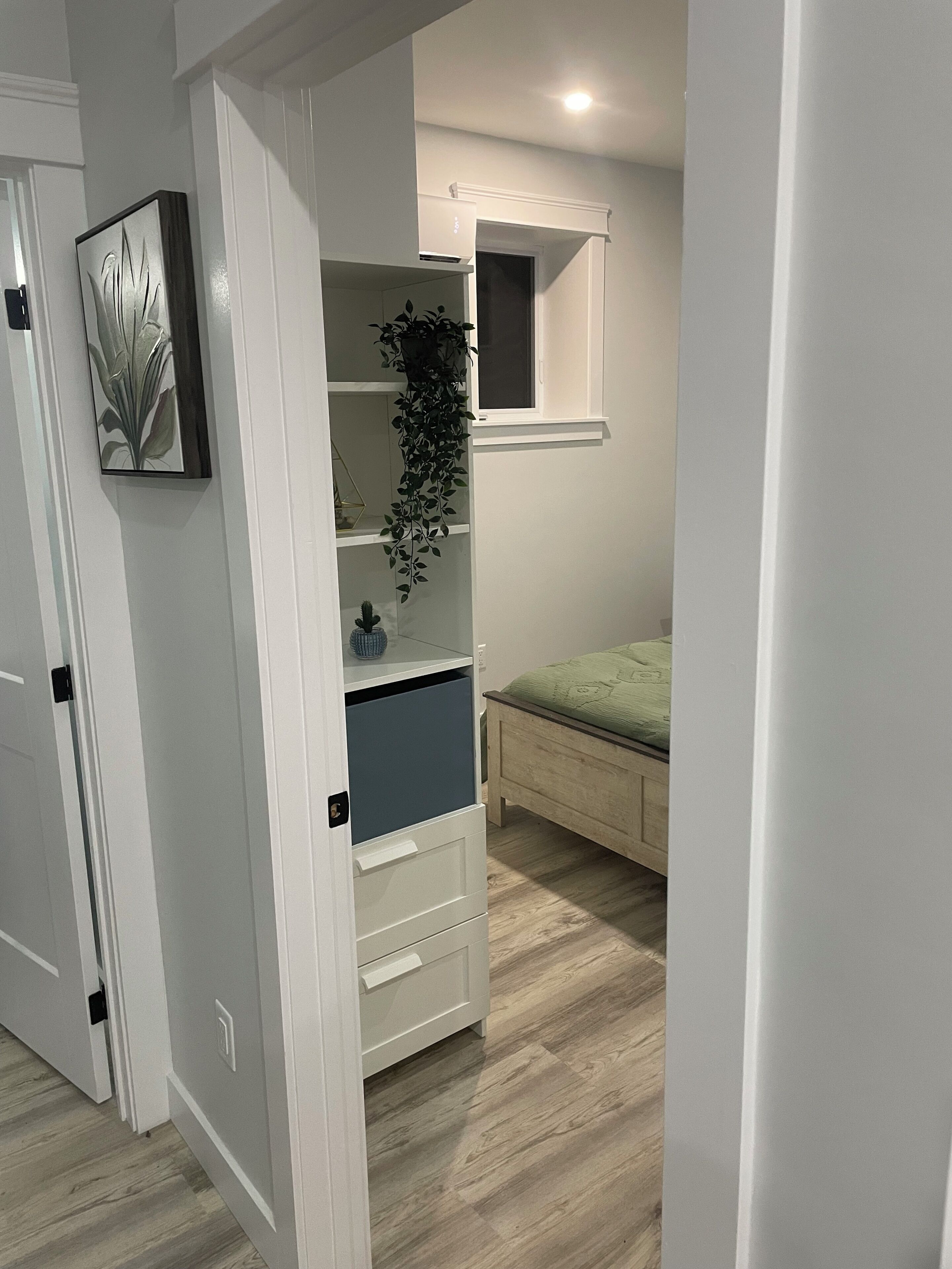 Une chambre à coucher avec un lit, une armoire blanche, une plante et une fenêtre.