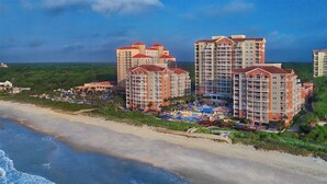 Un hotel frente al mar con varios edificios altos, un área de piscina y una playa.