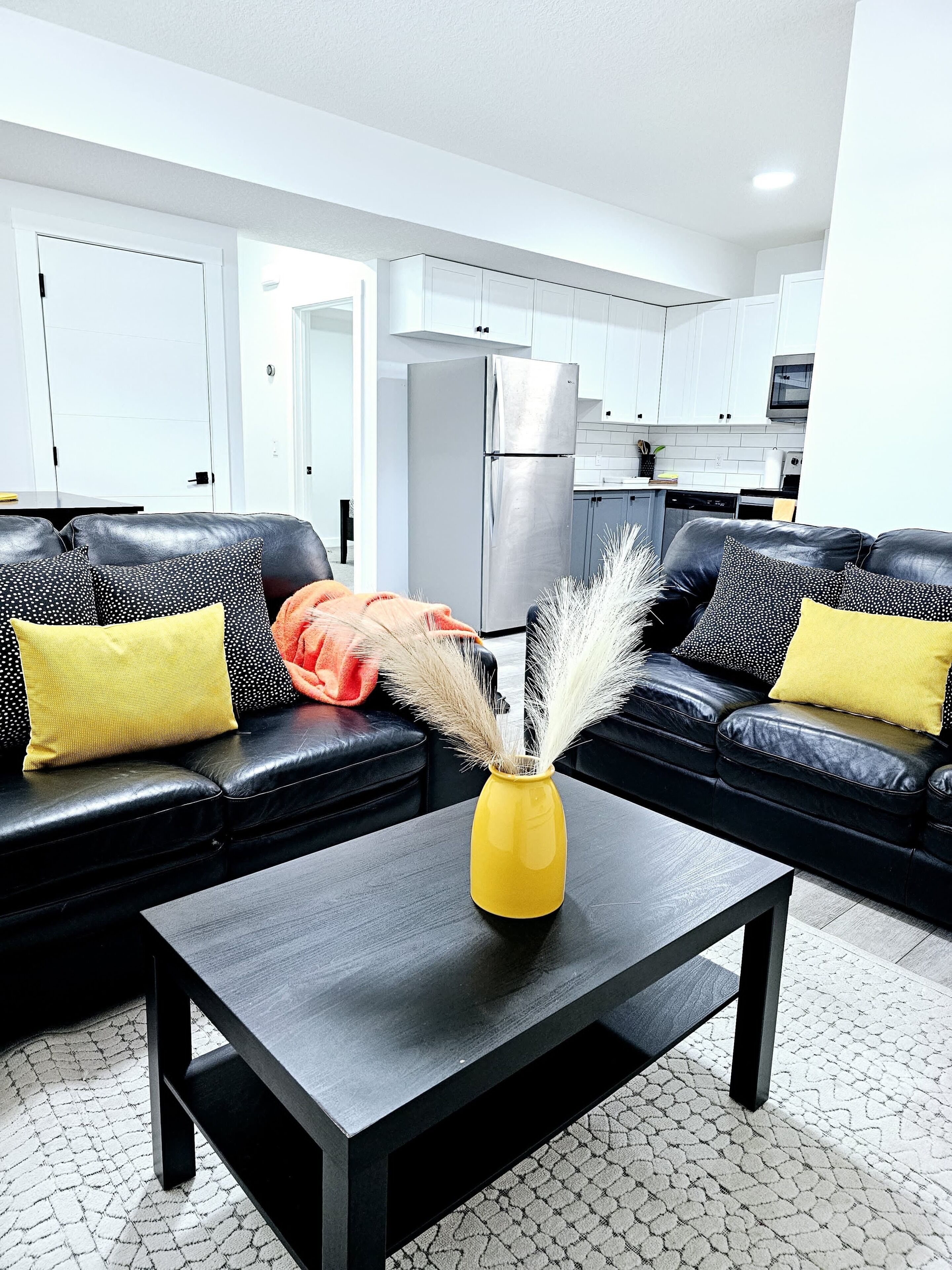 A modern living room with a black leather sofa, a yellow vase with pampas grass, and a dark coffee table.